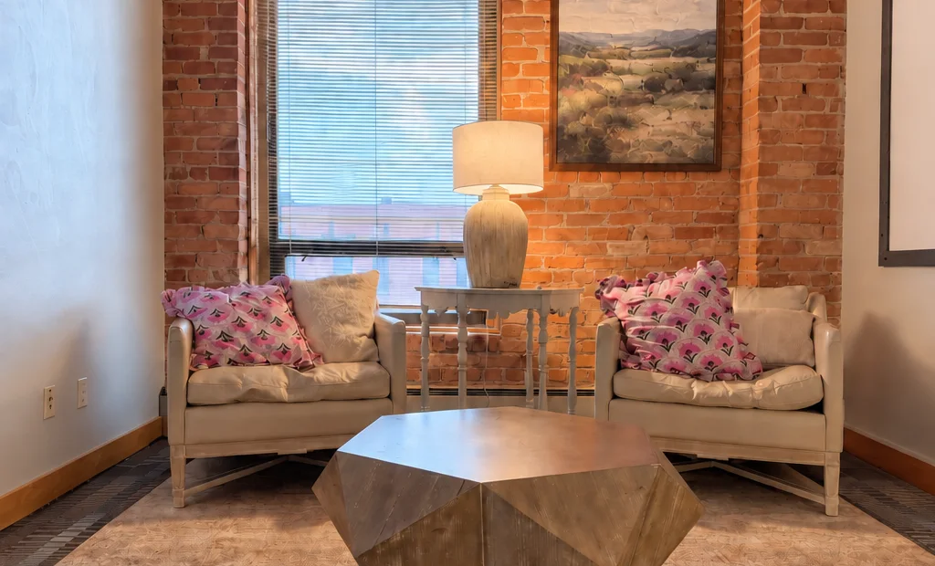 Two armchairs facing each other beside a brick wall and window in the couples room